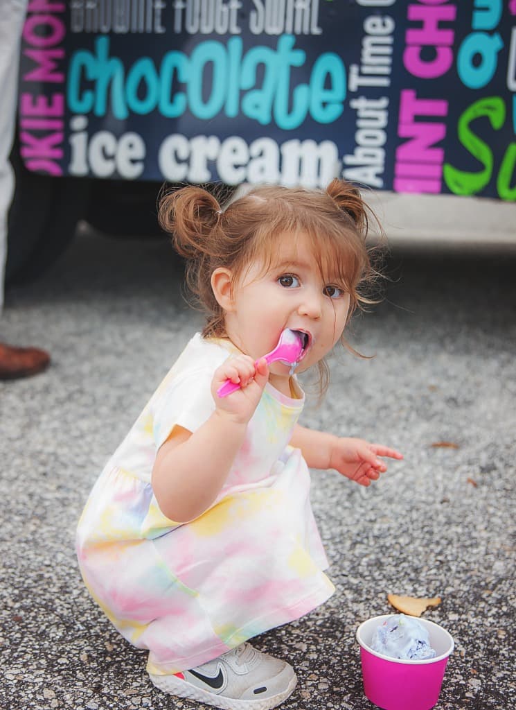 A toddler in a tie-dye dress eating ice cream beside the truck